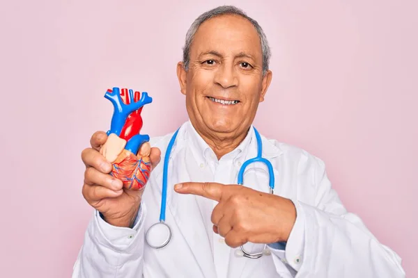 シニアHoary医師男身に着けていますStethoscope保持プラスチックハート上のピンクの背景非常に幸せなポインティングとともに手と指 — ストック写真