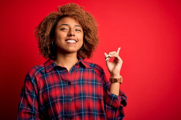 Young beautiful African American afro woman with curly hair wearing casual shirt with a big smile on face, pointing with hand and finger to the side looking at the camera.