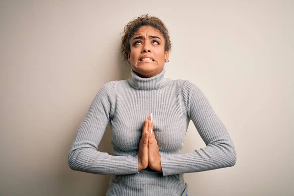 Beautiful african american girl wearing turtleneck sweater standing over white background begging and praying with hands together with hope expression on face very emotional and worried. Begging.