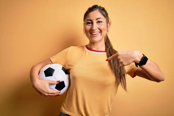 美しいですブルネットプレーヤー女性遊びサッカーボールを使用しています黄色の背景とともに驚き顔指して指へ彼自身 — ストック写真