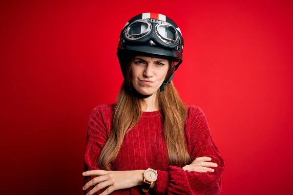 赤い背景の懐疑的で神経質な上に元ヘルメットを身に着けている若い美しい赤毛の元サイクリストの女性は 両腕を組んで顔に不承認の表現 負の人 — ストック写真