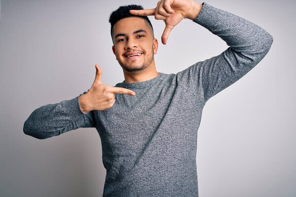 Young handsome man wearing casual sweater standing over isolated white background smiling making frame with hands and fingers with happy face. Creativity and photography concept.