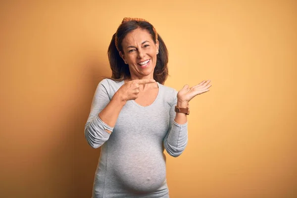 妊娠中の赤ちゃんを期待している中年の妊婦は驚きと笑顔でカメラに提示しながら手と指差しで指 — ストック写真