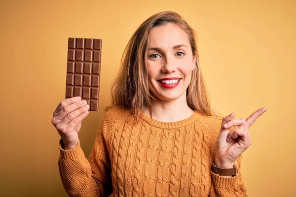 Jovem Mulher Loira Bonita Segurando Barra Chocolate Sobre Fundo Amarelo — Fotografia de Stock