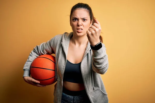 Junge Schöne Brünette Sportlerin Hält Basketballball Über Gelbem Hintergrund Genervt — Stockfoto