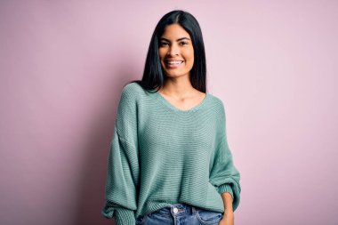 Moda kıyafetleri giyen genç ve güzel bir kadın. Manken, sokak tarzı giyiniyor. Pembe arka planda dikiliyor.