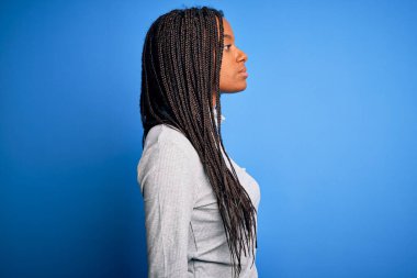 Genç Afro-Amerikalı kadın mavi izole edilmiş arka plan üzerine günlük balıkçı yaka giyen rahat bir görünüm ve kendine güvenen bir gülümseme takınıyor..