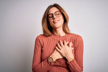 Genç, güzel, esmer bir kadın beyaz arka plan üzerine gözlük takmış göğsünde elleri kapalı gülümsemeler ve yüzünde minnet dolu bir jest ile. Sağlık kavramı.