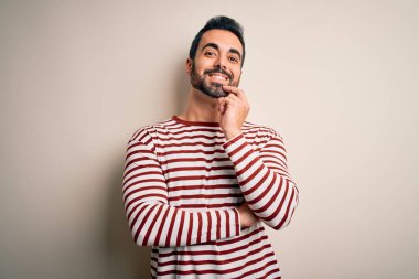 Sakallı, sıradan çizgili tişörtlü, beyaz arka planda duran, kameraya kendinden emin, kolları çapraz ve çenesi yukarıda gülümseyen genç yakışıklı bir adam. Olumlu düşünüyorum..