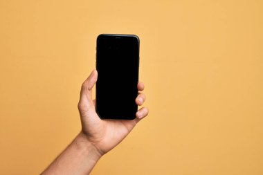 Kafkasyalı genç adam elinde akıllı telefonuyla izole edilmiş sarı arka planda ekranı gösteriyor.