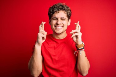 Sarışın, kıvırcık saçlı, kırmızı arka planda sıradan tişörtler giyen, umut ve gözler kapalı bir şekilde gülümseyen genç, yakışıklı bir adam. Şans ve batıl inanç..