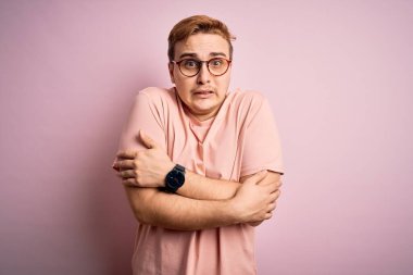 Genç, yakışıklı, günlük tişört giyen, pembe arka planda duran, kışın soğuktan titreyen ve soğuktan donan, yüzünde üzgün ve şok ifadesi olan bir adam.