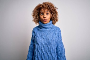 Beyaz arka plan üzerine balıkçı yaka kazak giyen genç ve güzel Afro-Amerikan kadın dudaklı balık suratı yapıyor, çılgınca ve komik bir jest. Komik ifade.