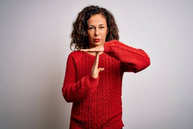 Orta yaşlı esmer kadın, günlük süveter giyer, izole edilmiş beyaz arka planda durur. Elleriyle hareket eder, hayal kırıklığına uğramış ve ciddi bir yüz ifadesi takınır.