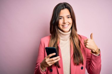 Genç, güzel bir kız beyaz arka plan üzerinde akıllı telefon kullanıyor. Gülümsüyor ve gülümsüyor. Tamam işareti yapıyor.