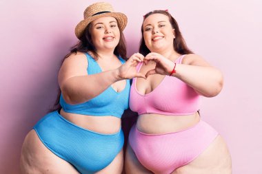 Sevgiyle gülümseyen bikini giyen genç ve büyük beden ikizler kalp sembolü ve elleri ile şekil veriyor. romantik kavram. 