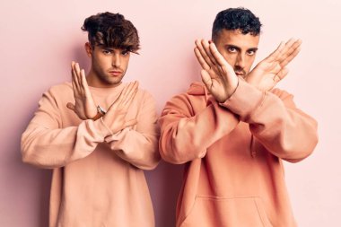 Gündelik giysiler giyen genç eşcinsel bir çift. Reddedilmiş yüz ifadesi. Kollarını kavuşturup negatif işaret veriyorlar. 