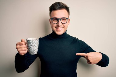 Genç, beyaz, gözlüklü bir adam. Bir fincan sıcak kahve içiyor ve kendini işaret ediyor.