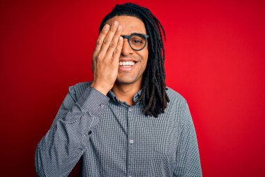 Rastgele gömlek ve gözlük takan, bir gözünü elinle kapatan, yüzünde kendine güvenen gülümseyen ve sürpriz duygular besleyen Afro-Amerikan genç adam..