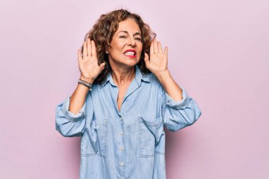 Orta yaşlı, güzel bir kadın pembe arka planda dikilmiş sıradan bir kot gömlek giyiyor. İki elini de kulak hareketi yaparken duymaya çalışıyor. Dedikoduya meraklı. İşitme problemi, sağır