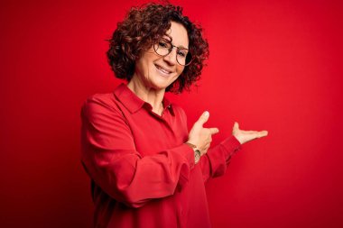 Orta yaşlı, kıvırcık saçlı, rahat gömlekli, kırmızı arka planda gözlüklü güzel bir kadın gülümseyerek içeri girmeye davet ediyor.