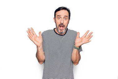 Orta yaşlı, çizgili tişört giyen yakışıklı bir adam izole edilmiş beyaz arka planda duruyor ve kolları açık, hiçbir fikri ve şüpheli bir yüzü yok..