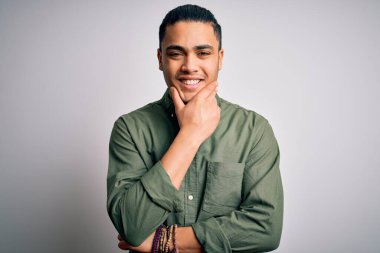 İzole edilmiş beyaz arka plan üzerinde duran Brezilyalı genç adam çapraz kollar ve çeneyle gülümseyen kameraya kendinden emin bir şekilde bakıyor. Olumlu düşünüyorum..