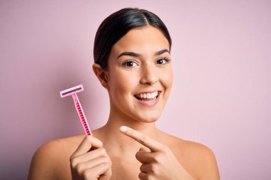 Tıraş makinesi kullanan genç ve güzel bir kız soyutlanmış pembe arka planda el ve parmaklarıyla mutlu mesut duruyor.
