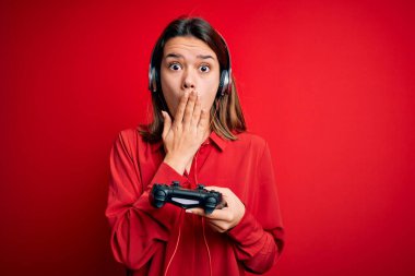 Oyun oynayan güzel esmer kız joystick ve kulaklıkla oyun oynuyor. Ağzını kapatıyor. Utancından ağzı açık kalıyor, korku ifadesi, sessizlikten korkmak, gizli konsept.