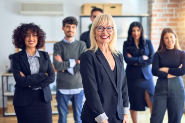 Bir grup iş adamı mutlu ve kendinden emin gülümsüyor. Birlikte poz verip kameraya bakıyoruz. Orta yaşlı, güzel bir kadın. Ofiste gülümsüyor.