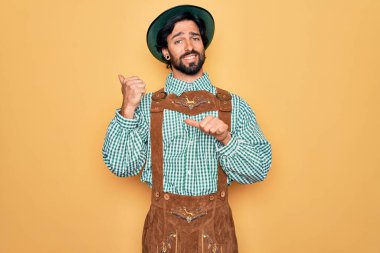 Almanya Festivali için geleneksel Alman Ekim Festivali adetleri giyen genç yakışıklı adam, elleri ve başparmakları havada, kendinden emin gülümsüyor.