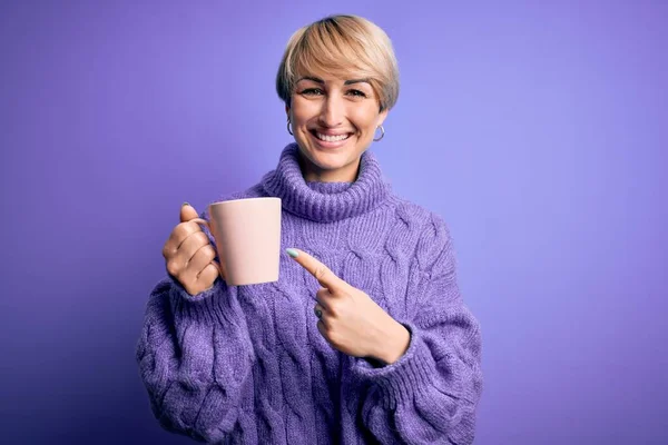 스웨터를 머리의 금발의 여자는 손가락으로 가리키며 커피를 마신다 — 스톡 사진