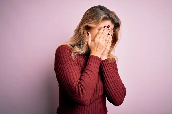 Young beautiful blonde woman wearing casual sweater over isolated pink background with sad expression covering face with hands while crying. Depression concept.