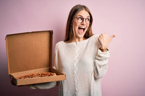 美しいです赤毛女性保持デリバリーボックスとともにイタリアの新鮮なピザ以上ピンクの背景ポインティングとショーで親指で側まで幸せな顔笑顔 — ストック写真