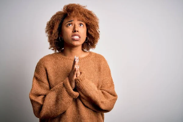 Young beautiful African American afro woman with curly hair wearing casual sweater begging and praying with hands together with hope expression on face very emotional and worried. Begging.