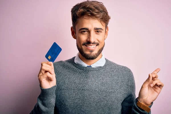 若いです顧客男とともに髭を保持クレジットカードのために支払い上のピンクの背景非常に幸せなポインティングで手と指で側面 — ストック写真