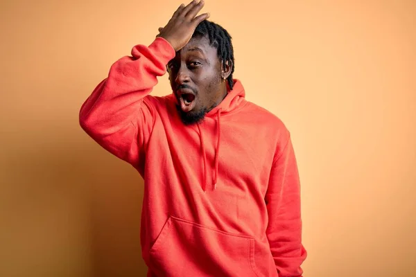 Young african american sporty man wearing sweatshirt with hoodie over yellow background surprised with hand on head for mistake, remember error. Forgot, bad memory concept.