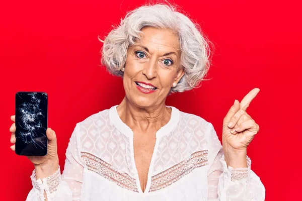 Starsza Siwowłosa Kobieta Trzyma Zepsuty Smartfon Pokazując Pęknięty Ekran Uśmiechnięty — Zdjęcie stockowe