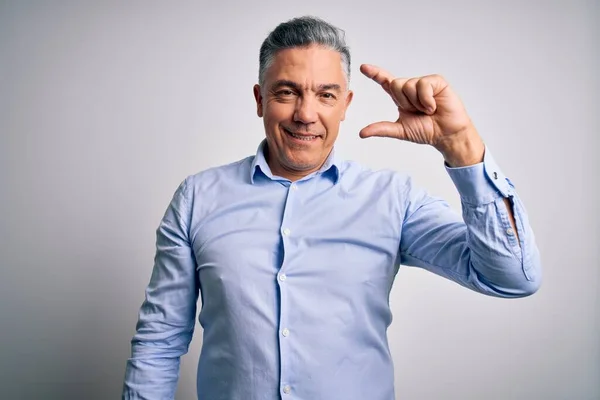 Middle age handsome grey-haired business man wearing elegant shirt over white background smiling and confident gesturing with hand doing small size sign with fingers looking and the camera. Measure concept.