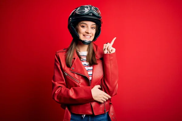 若い美しいブルネットの元サイクリストの女性は カメラを見ている側に手と指で指して 顔に大きな笑顔でオートバイのヘルメットと赤いジャケットを着て — ストック写真