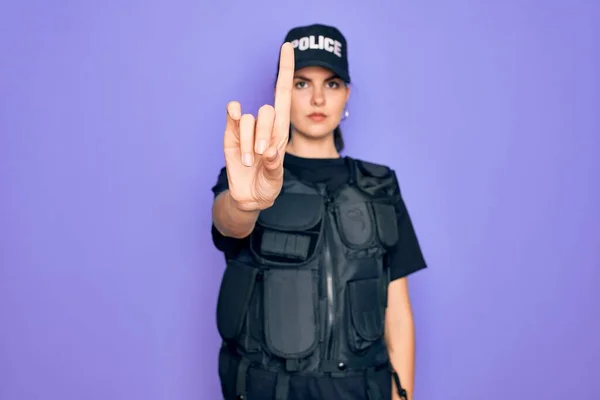 Young police woman wearing security bulletproof vest uniform over purple background Pointing with finger up and angry expression, showing no gesture