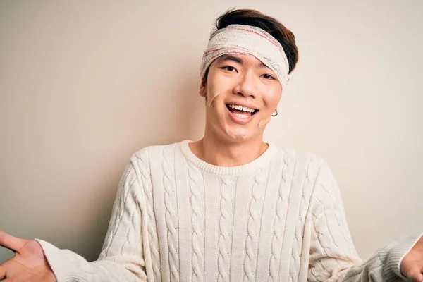 Young handsome chinese man injured for accident wearing bandage and strips on head smiling cheerful offering hands giving assistance and acceptance.