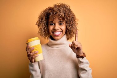 Genç Afro-Amerikalı kıvırcık kadın sarı arka planda bir fincan kahve içerken bir fikir ya da soru işareti ile şaşırdı.