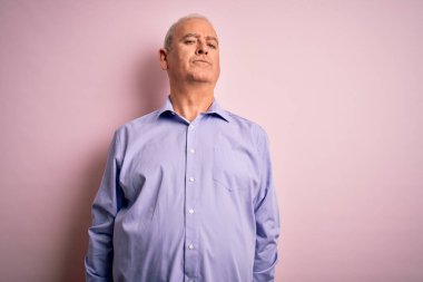 Orta yaşlı, yakışıklı, beyaz gömlekli, pembe arka planda duran, yüzünde ciddi bir ifadeyle rahatlamış bir adam. Basit ve doğal bir şekilde kameraya bakıyorsun..