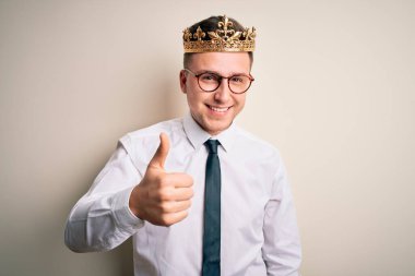 Soyutlanmış arka planda altın taç takan yakışıklı beyaz iş adamı mutlu bir el hareketi yapıyor. Kameraya bakıp başarıyı gösteren ifade onaylanıyor.