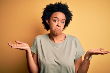 Kıvırcık saçlı, sıradan tişörtsüz, kafası karışık ve kolları ve elleri havada, Afro-Amerikan bir kadın. Şüphe kavramı.