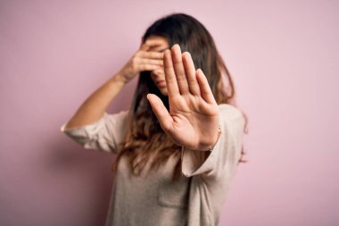 Genç, güzel, esmer bir kadın pembe arka planda dikiliyor, gözleri ellerle örtüyor ve üzgün ve korku dolu ifadelerle jest yapıyor. Utanç verici ve olumsuz bir kavram..