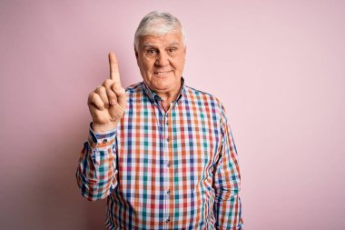 Tecrit edilmiş pembe arka plan üzerine gündelik tişört giyen kıdemli yakışıklı beyaz adam başarılı bir fikri işaret ediyor. Heyecanlı ve mutlu. Bir numara..