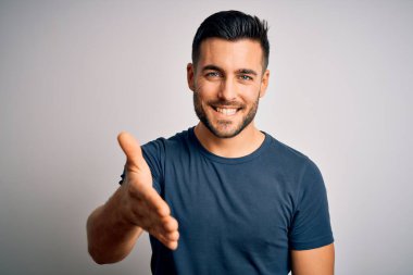 İzole edilmiş beyaz arka planda duran sıradan tişört giyen yakışıklı genç adam selamlaşma ve dostça bir şekilde tokalaşıyor. Başarılı bir iş..