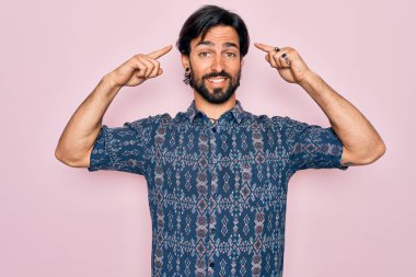 Pembe arka planda hippi tarzı giyinmiş genç, yakışıklı, bohem bir adam iki eliyle başını gösteren gülümseme, harika bir fikir ya da düşünce, iyi bir hafıza